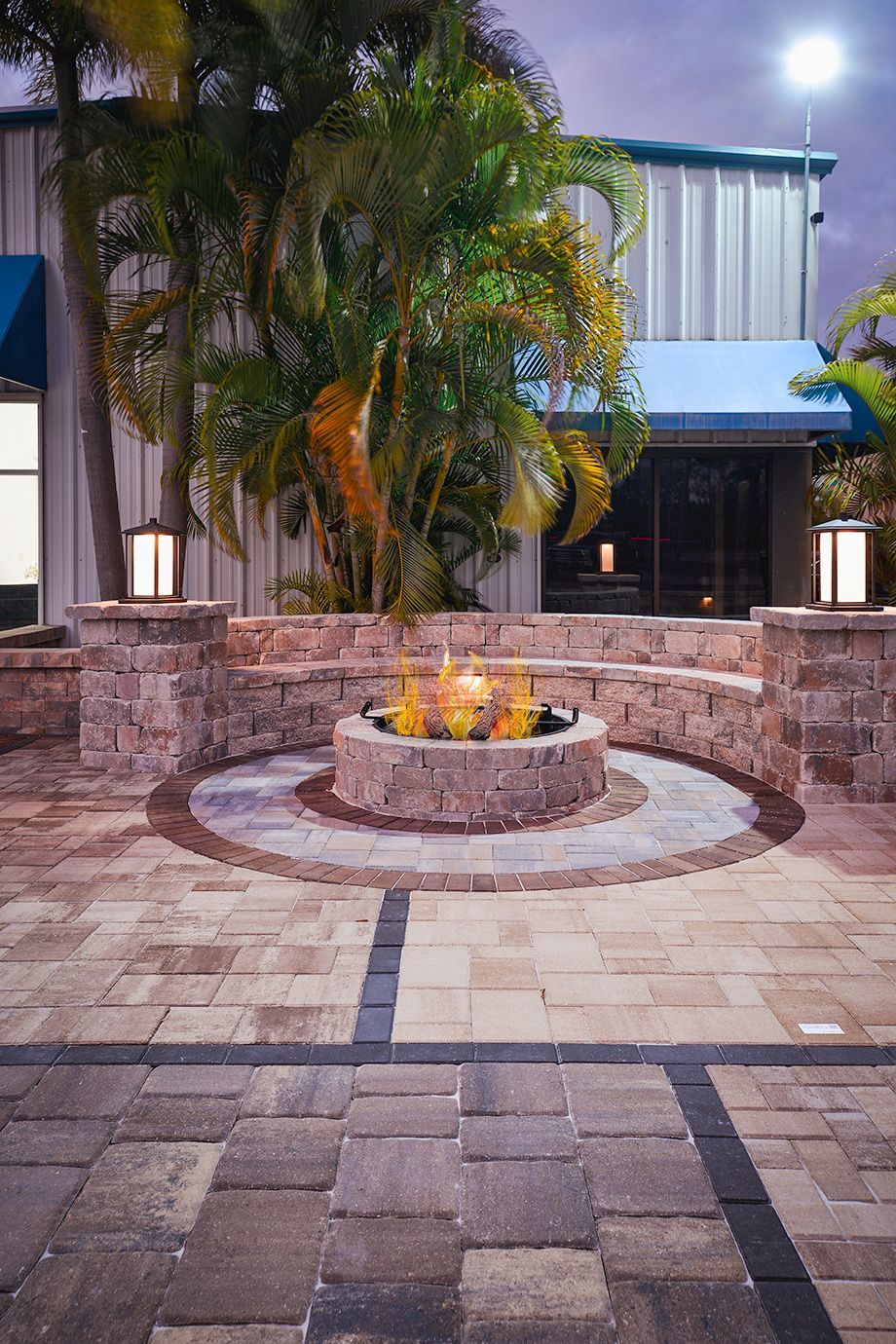 A fire pit is in the middle of a brick patio in front of a building.