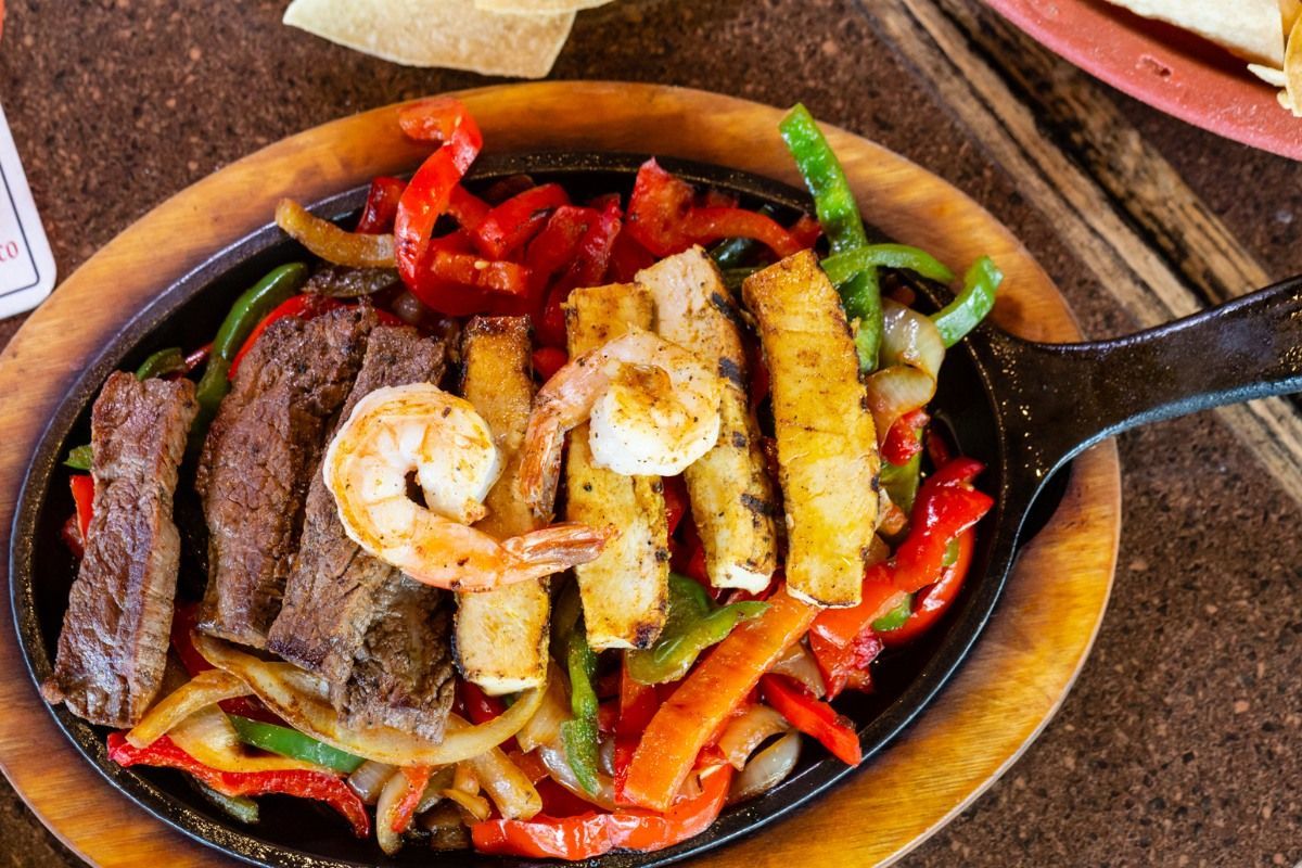 A skillet filled with steak , shrimp , peppers , onions and pineapple.