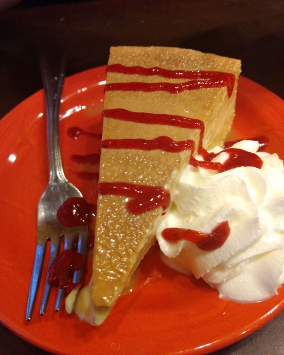 A slice of pie with whipped cream and strawberry sauce on an orange plate