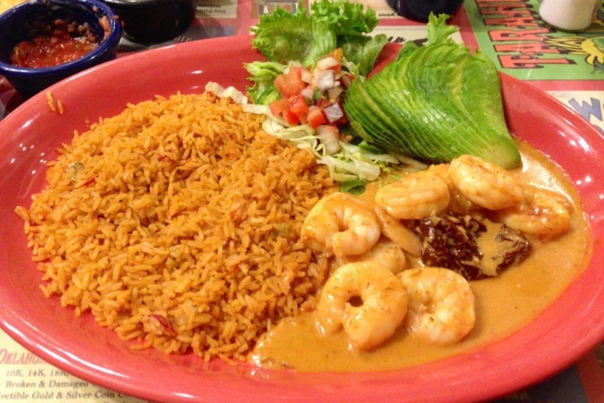 A plate of food with rice , shrimp and avocado on a table.