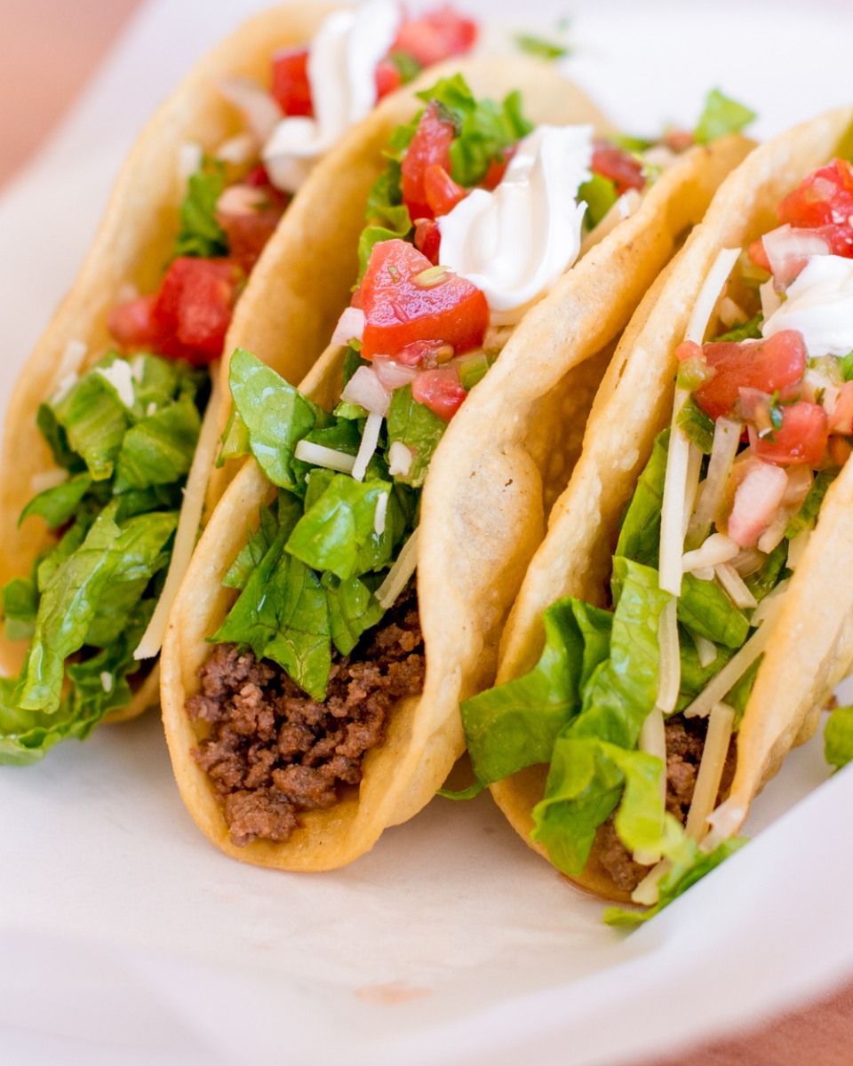 A close up of three tacos on a white plate