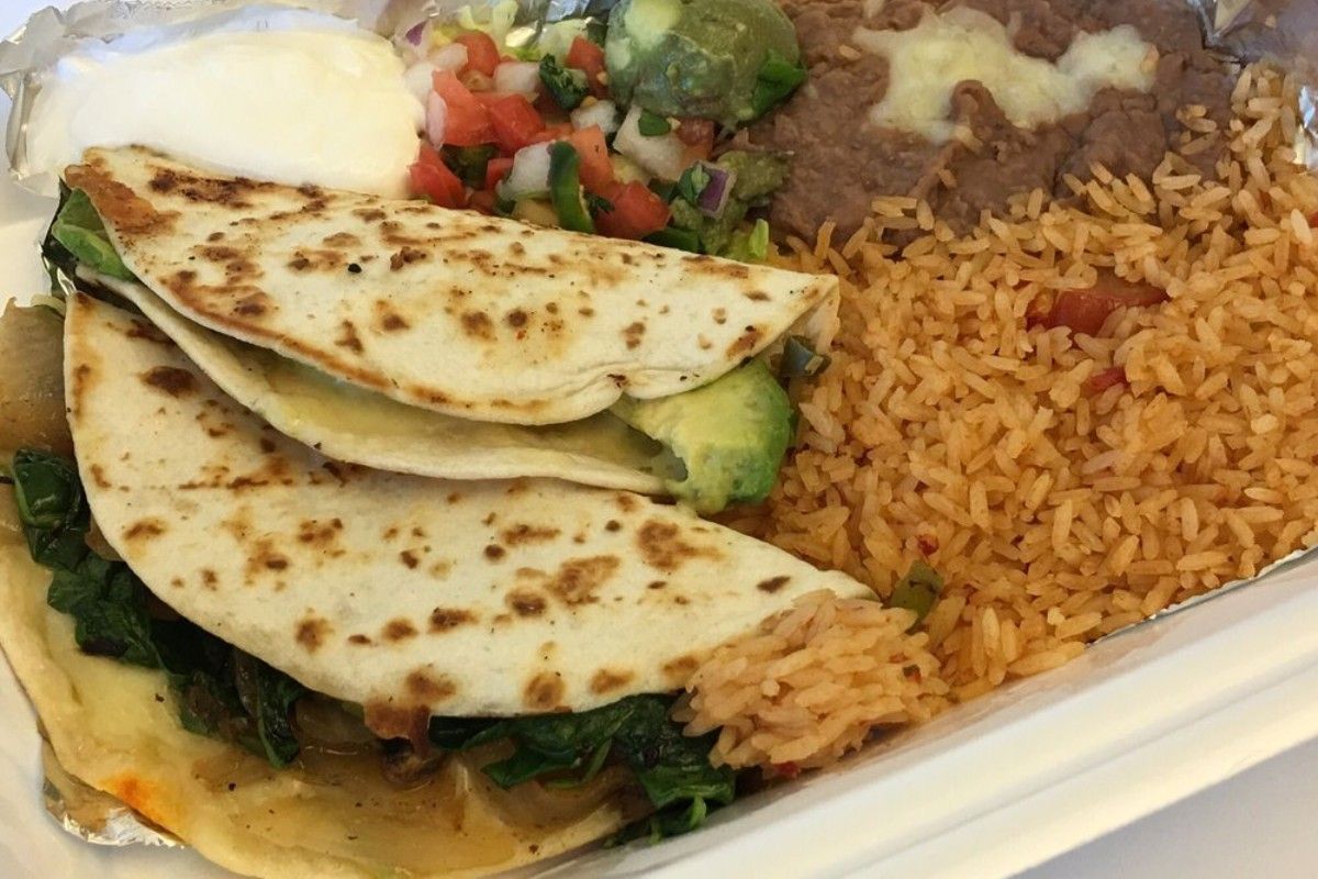 A close up of a quesadilla with rice and beans on a plate.