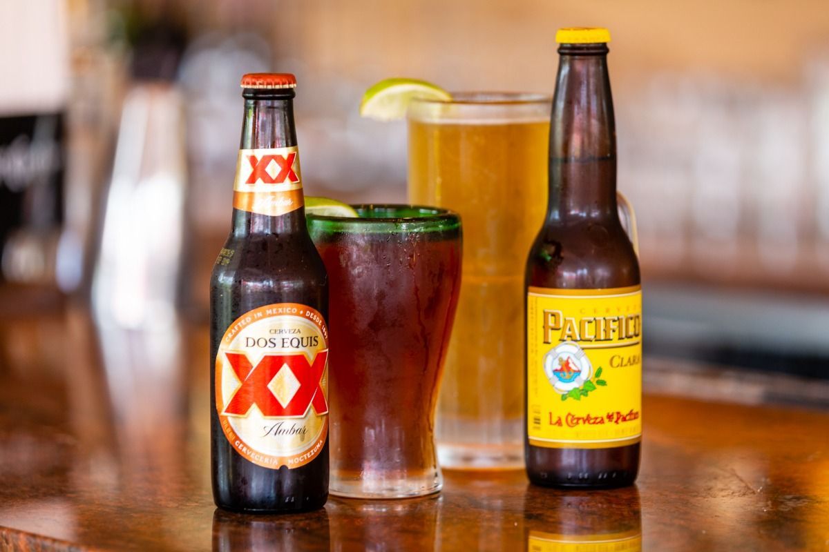 Three bottles of beer and two glasses of beer are on a bar.