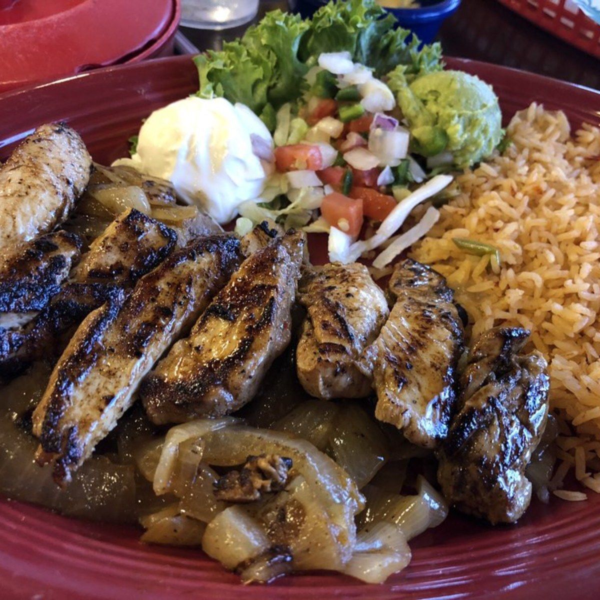 A red plate topped with grilled chicken and rice