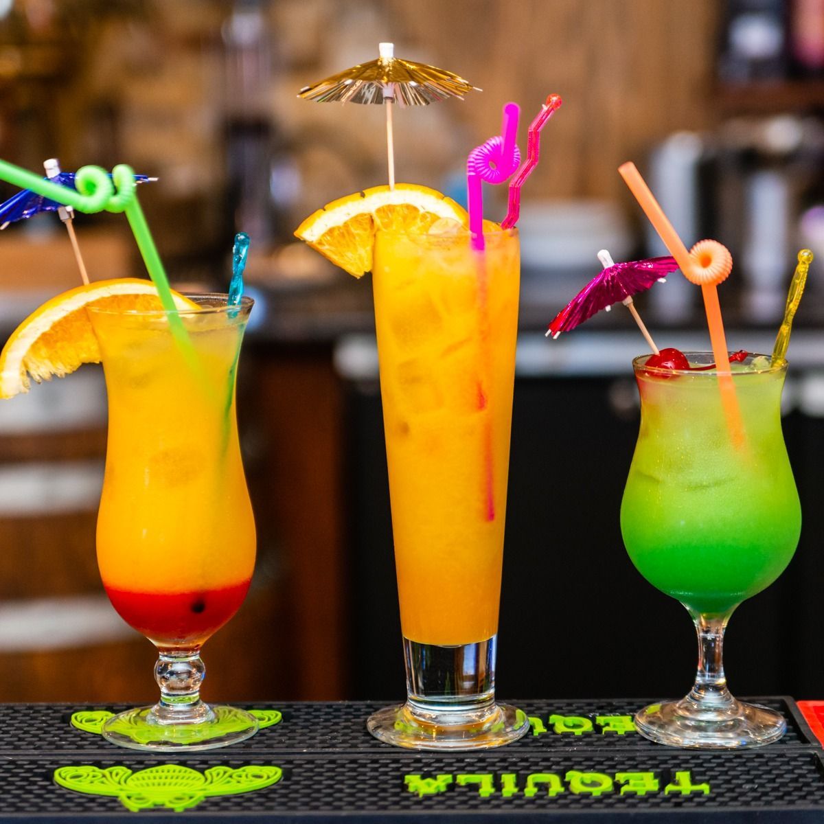 Three different colored drinks are on a bar that says tequila