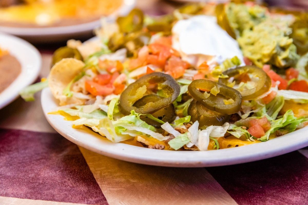 A close up of a plate of nachos with jalapenos and sour cream on a table.