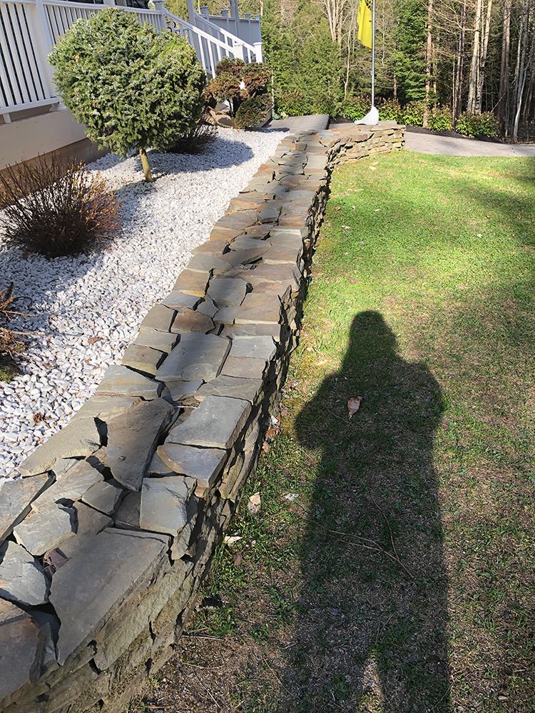 A shadow of a person is cast on a stone wall in a garden.
