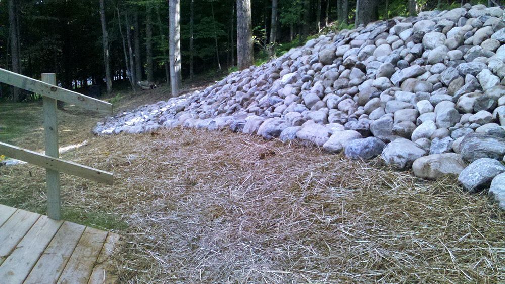 A large pile of rocks is sitting next to a wooden fence.