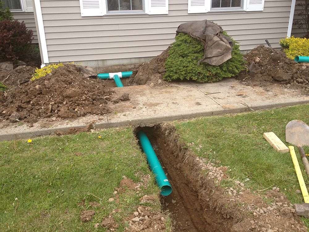 A green pipe is being installed in the dirt in front of a house.