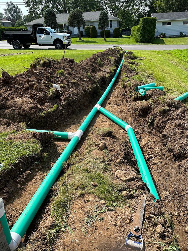 A white truck is parked next to a pile of green pipes in the dirt.