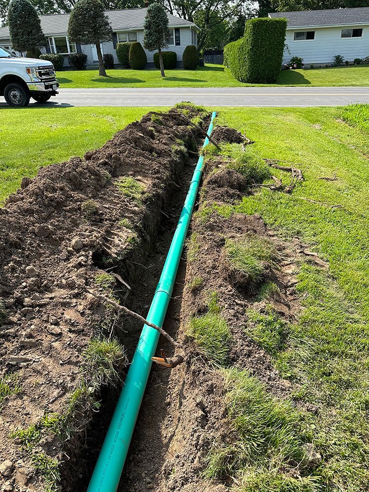 A green pipe is being installed in a trench next to a house.