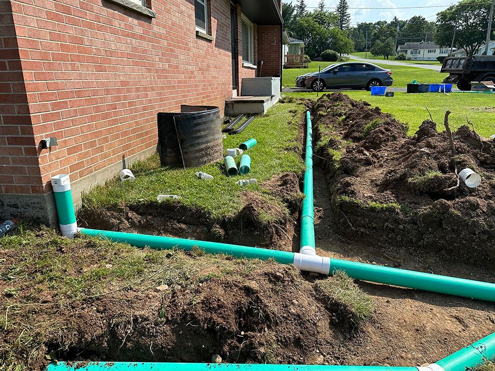 Green pipes are being installed in the dirt in front of a brick house.