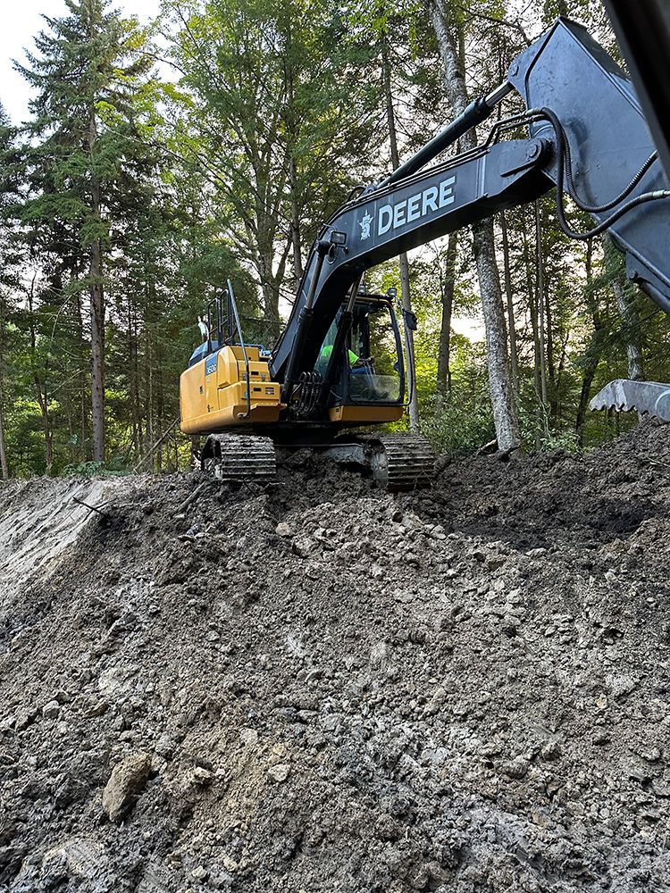 A deere excavator is sitting on top of a pile of dirt.