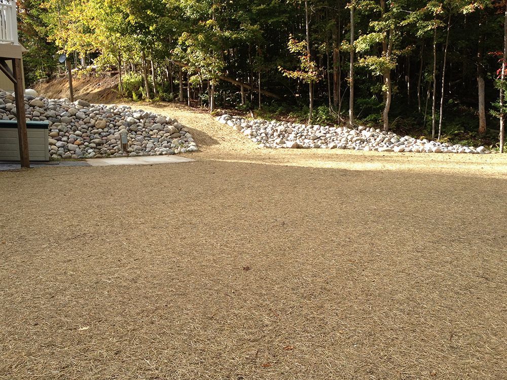A gravel driveway with trees in the background and a pile of rocks in the foreground.