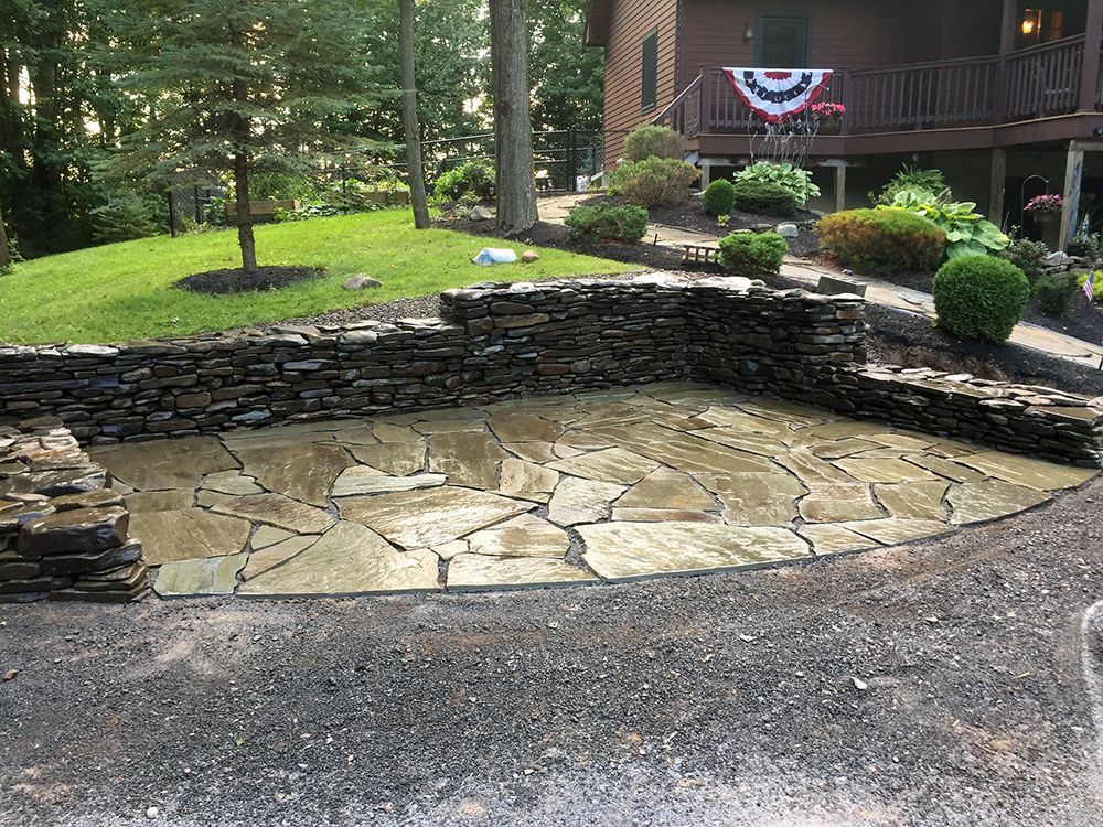 A stone wall surrounds a patio in front of a house.