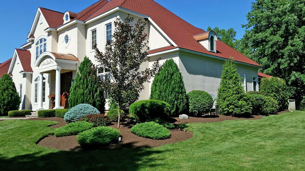 A large white house with a red roof is surrounded by trees and bushes.