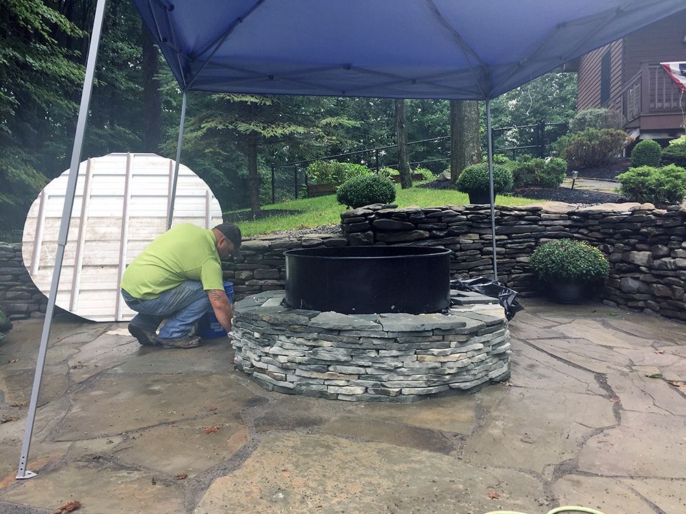 A man is working on a fire pit under a blue tent.