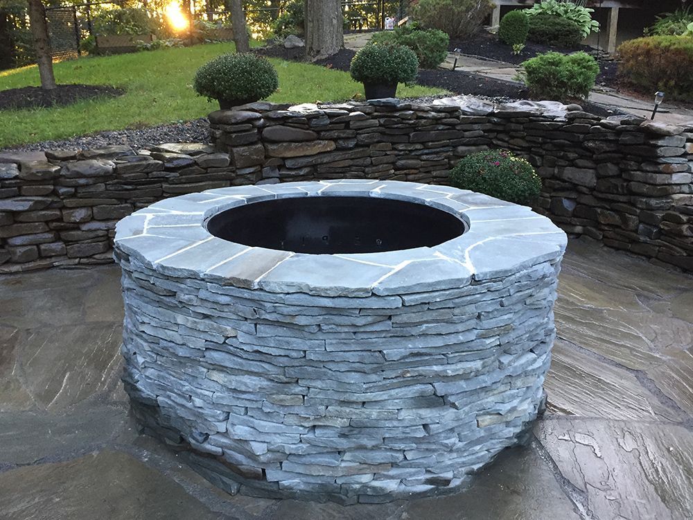 A stone fire pit is sitting on a patio next to a stone wall.