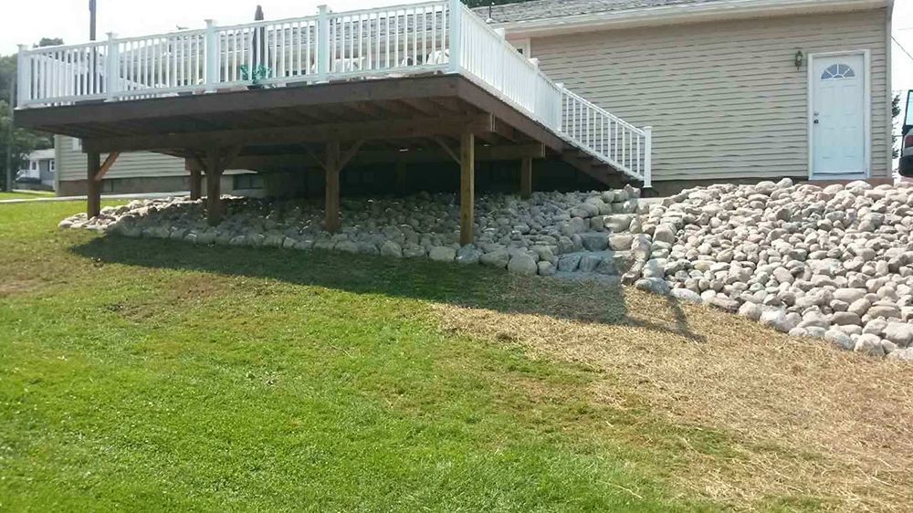 A large deck is sitting on top of a rocky hill next to a house.
