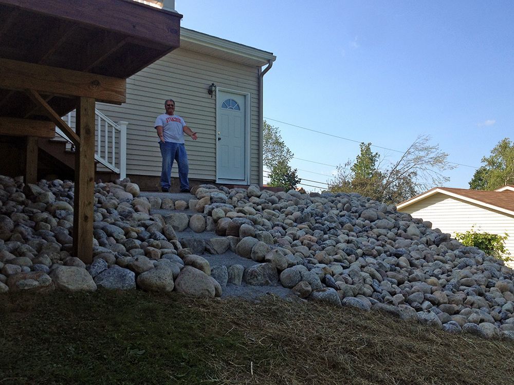 A man standing next to a pile of rocks in front of a house.