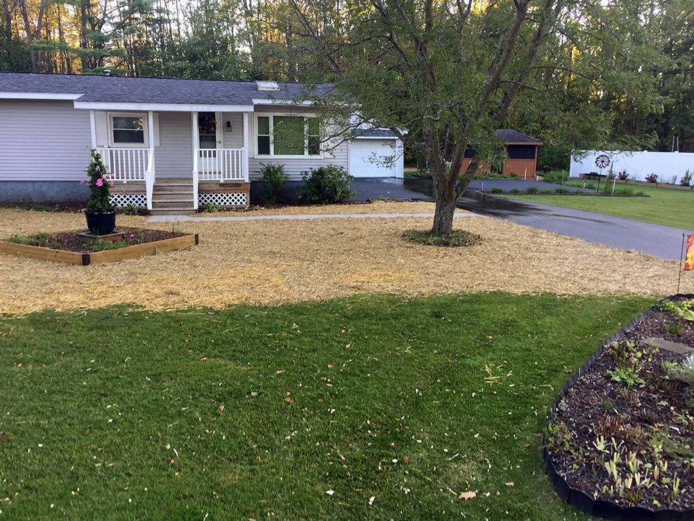 A white house with a porch and a gravel driveway in front of it.