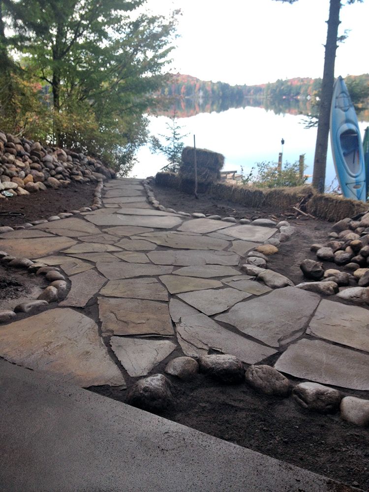 A stone walkway leading to a lake with a blue kayak in the background