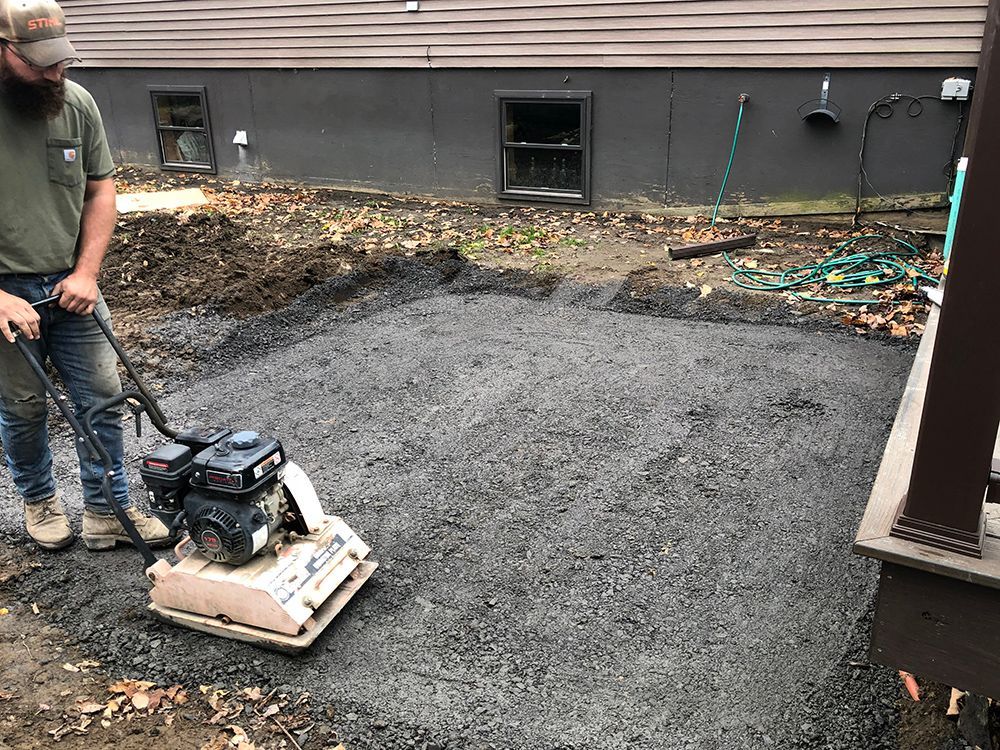 A man is using a machine to compact asphalt in a backyard.