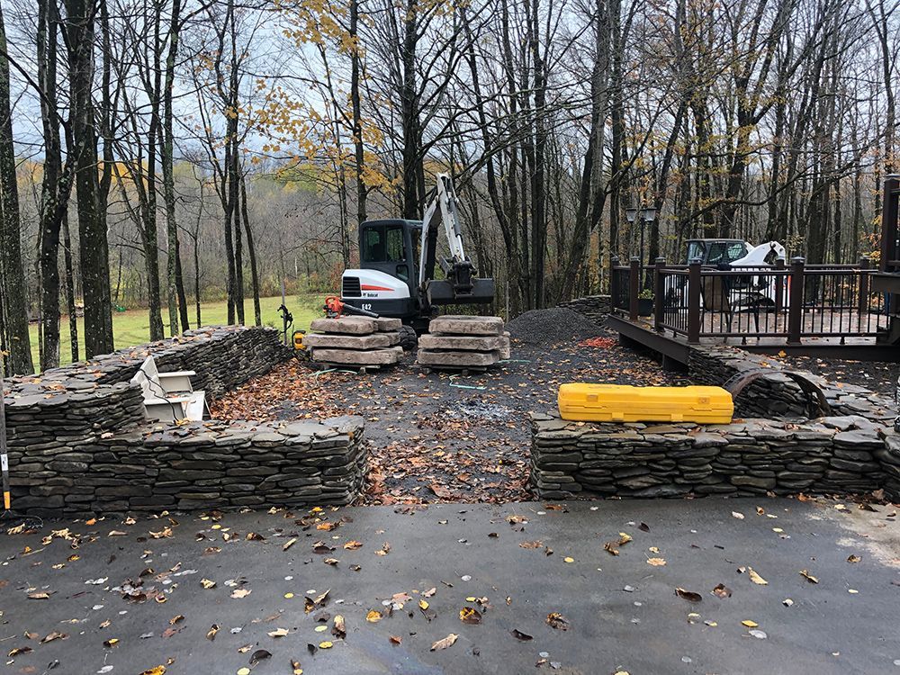 A bulldozer is working on a stone wall in the woods.