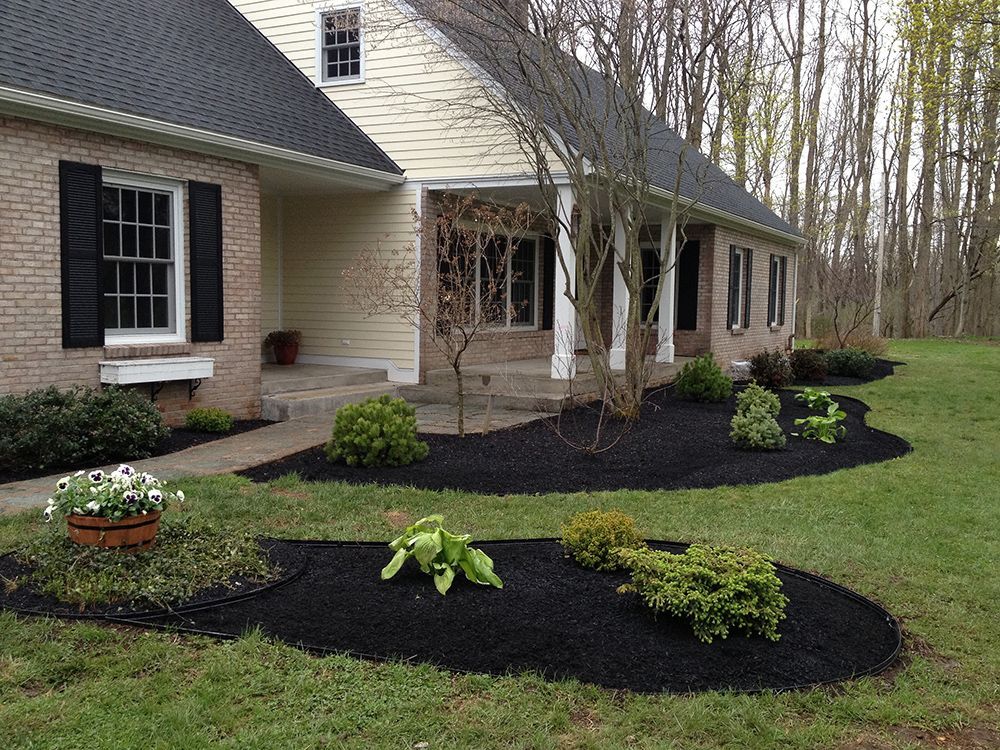 A white house with black shutters and black mulch in front of it