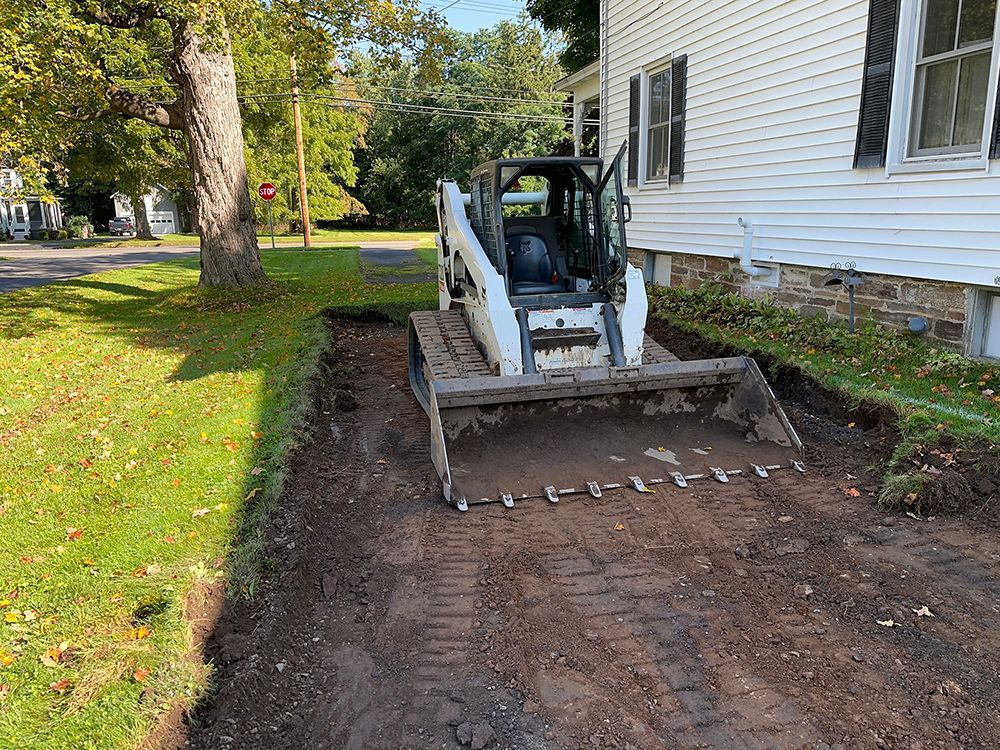 A bobcat is digging a hole in front of a house.