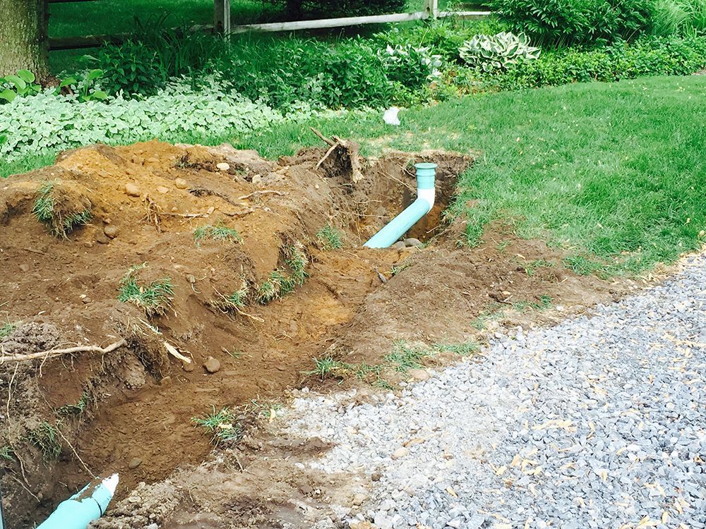 A blue pipe is being installed in the dirt next to a gravel road.