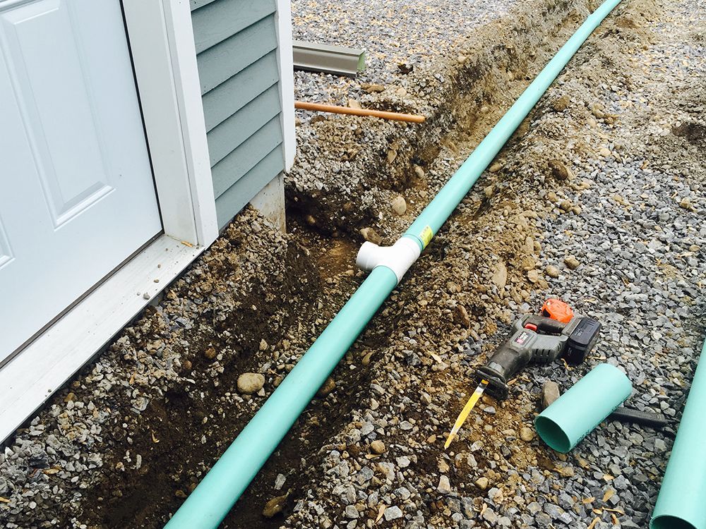 A green pipe is laying in the dirt next to a house