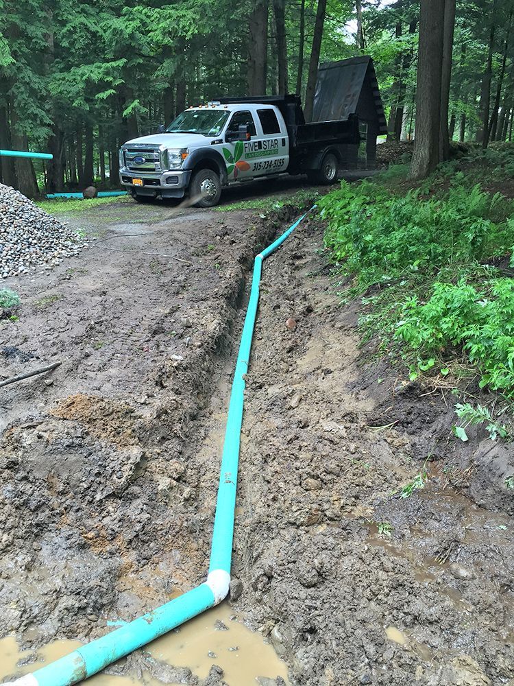 A truck is parked on the side of a dirt road next to a green pipe.