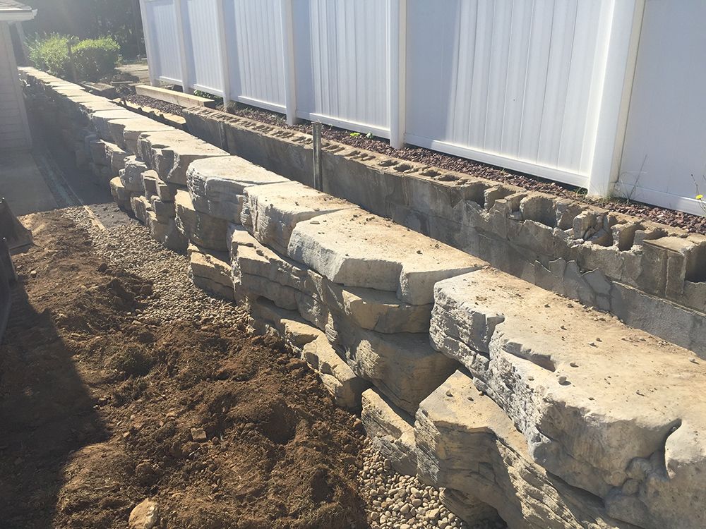 A stone wall is being built next to a white fence.