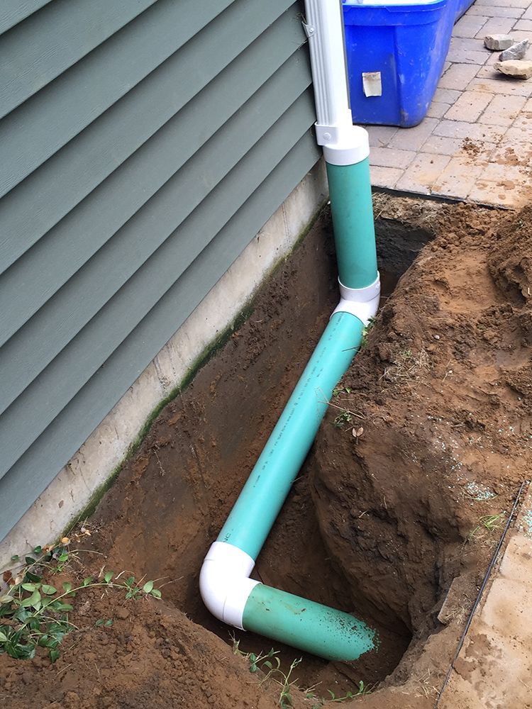 A green pipe is in the dirt next to a house