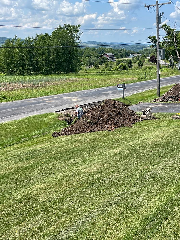A large pile of dirt is sitting on the side of a lush green field next to a road.