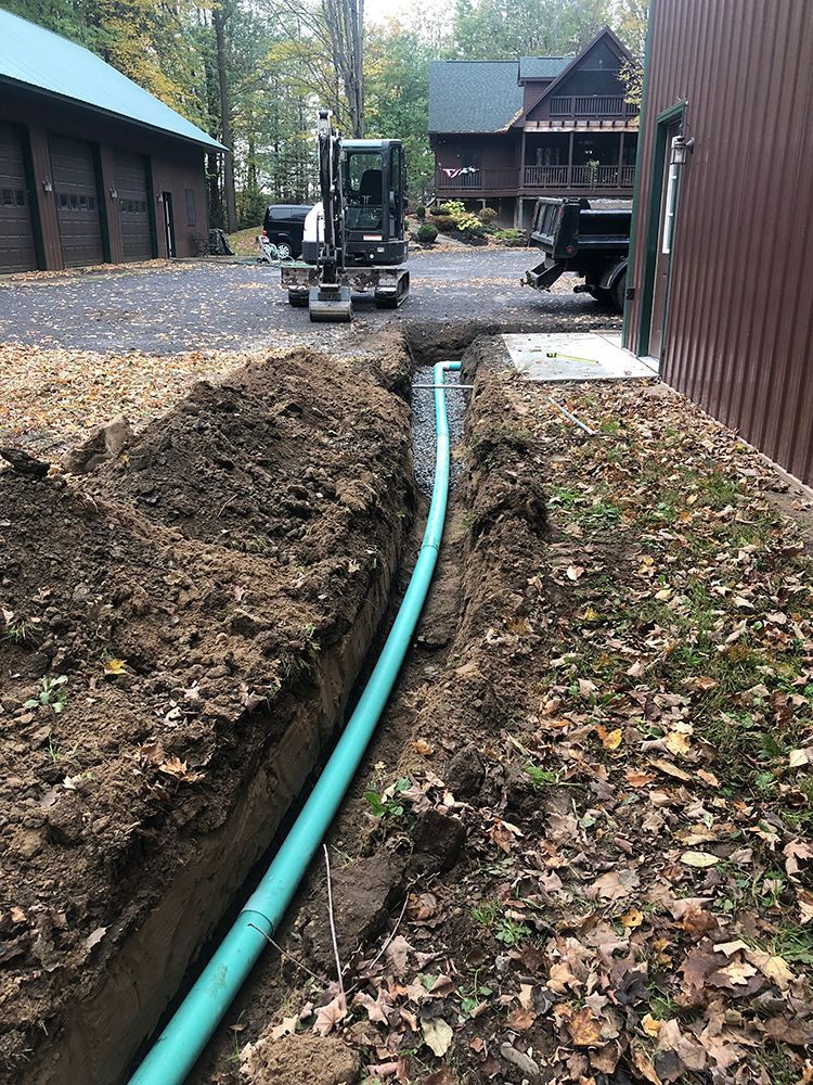 A green pipe is being installed in the dirt in front of a house.