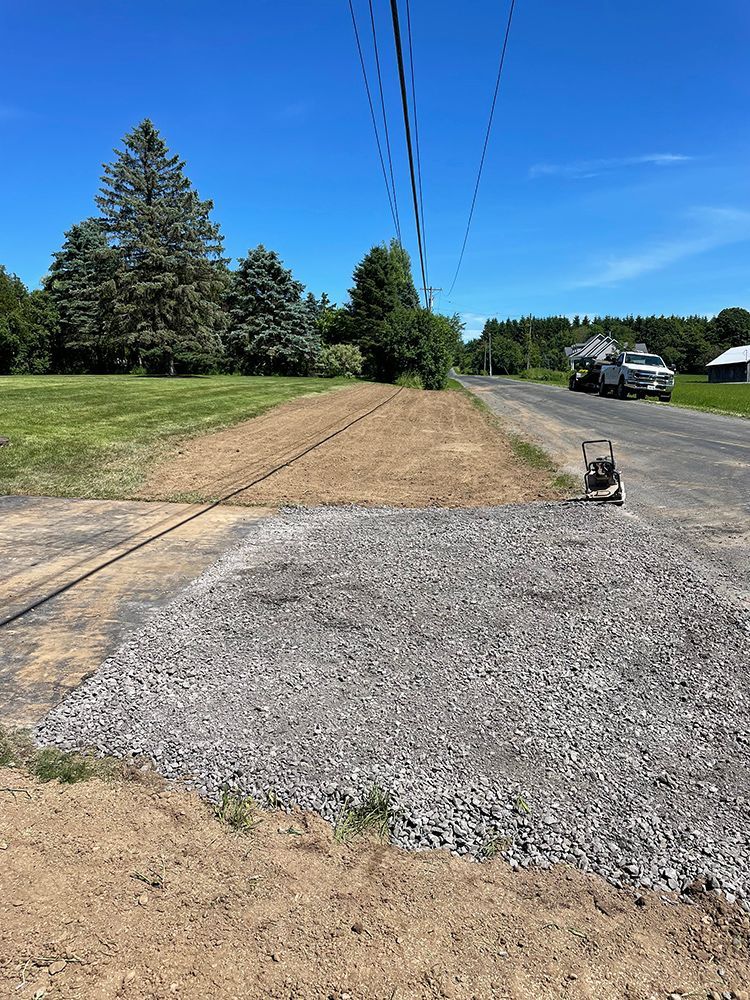 A gravel road going through a grassy field next to a road.