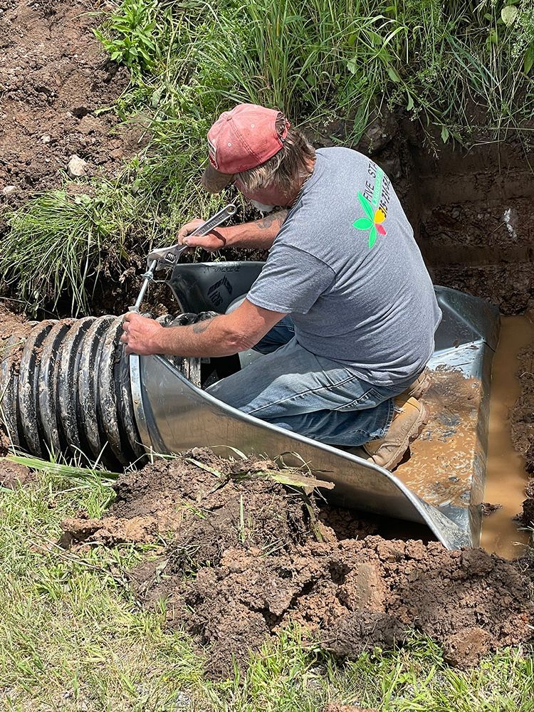 A man is kneeling in the dirt working on a pipe.