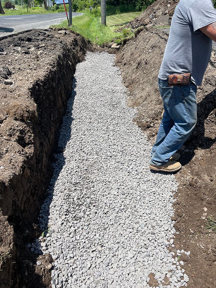 A man is standing in a trench filled with gravel.