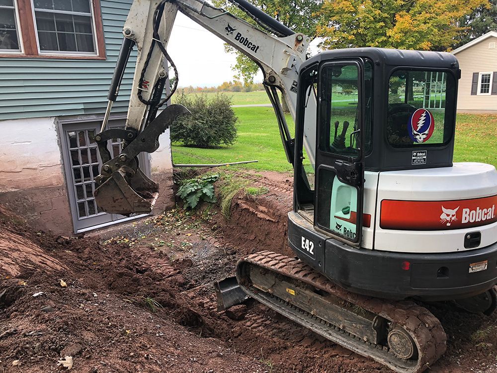 A bobcat excavator is digging a hole in front of a house.