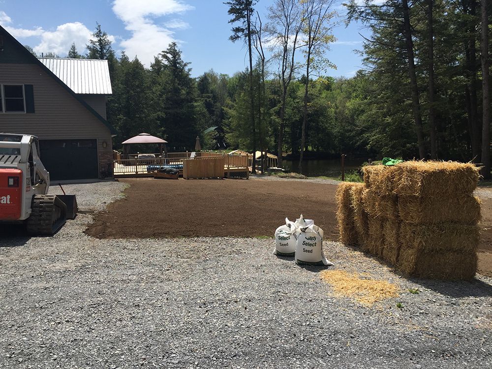 A bulldozer is parked in a gravel driveway next to bales of hay