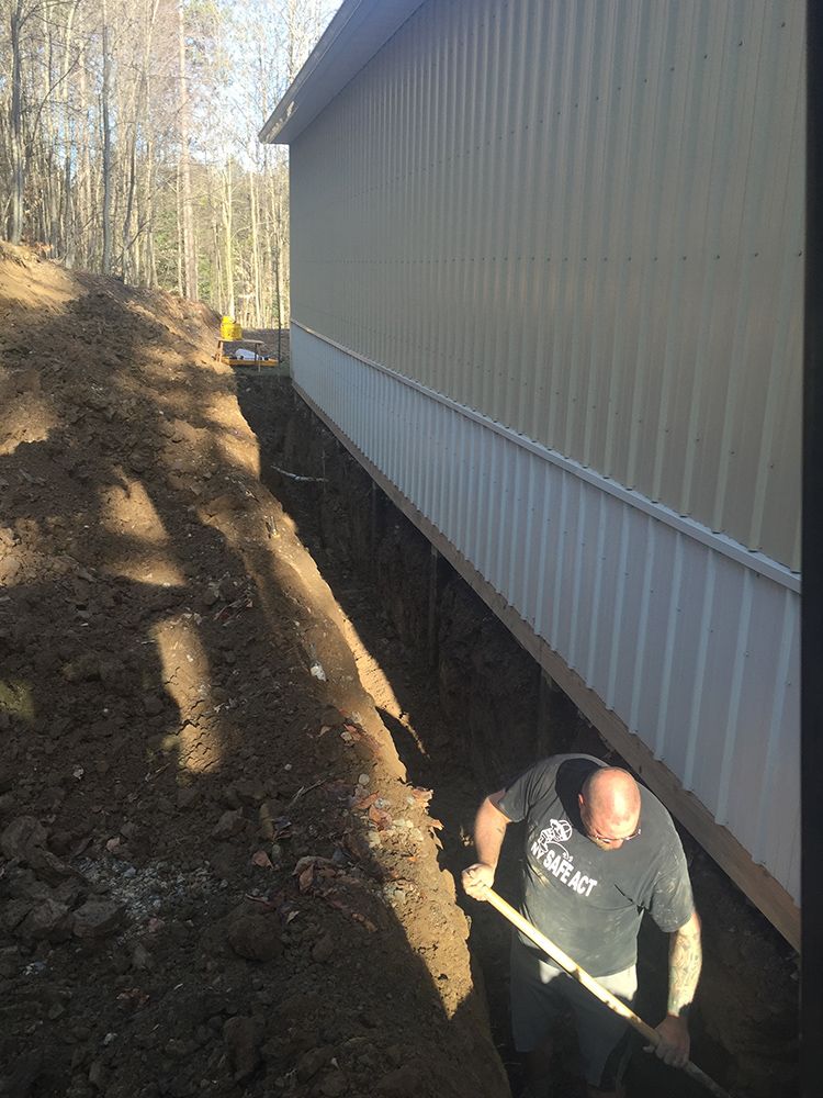 A man is digging a hole in the ground next to a building.