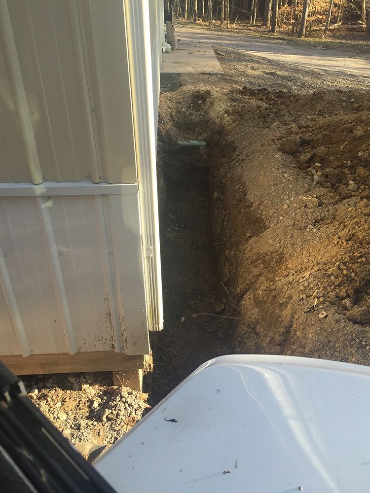 A white truck is driving down a dirt road next to a building.