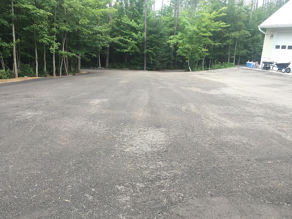 A large parking lot with trees in the background and a house in the background.