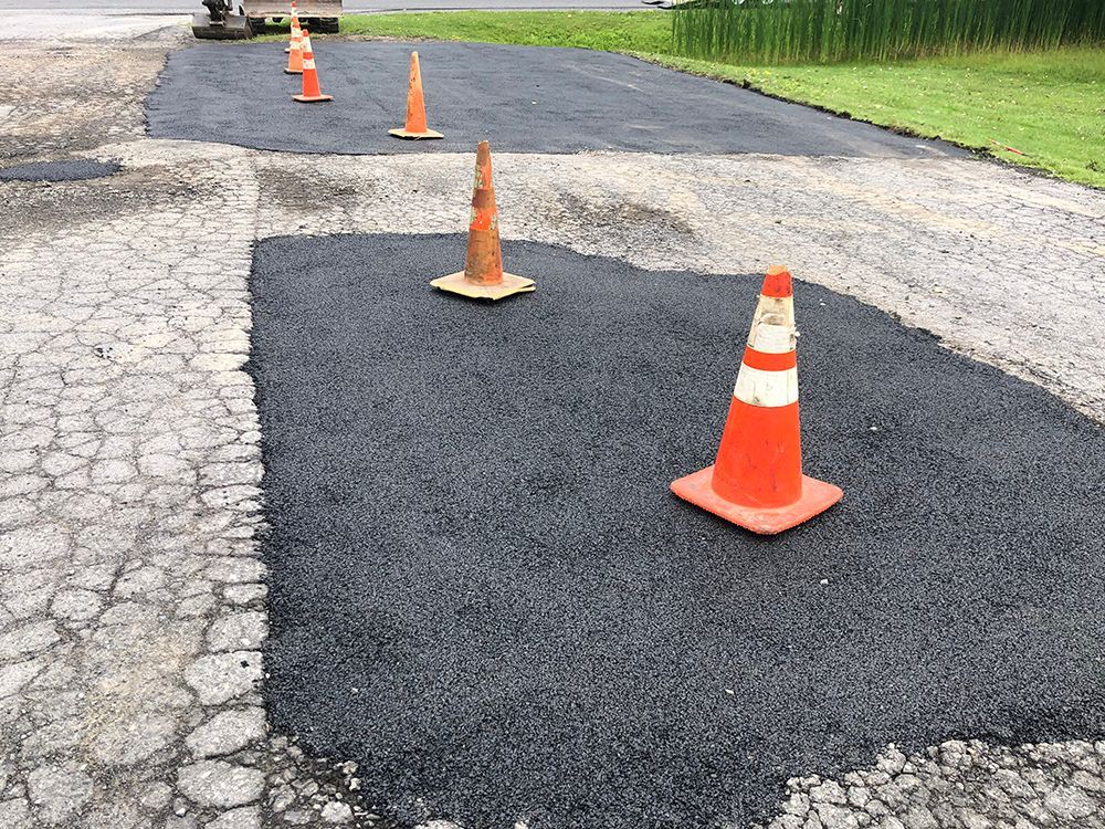 A row of orange and white traffic cones sitting on top of a black asphalt road.