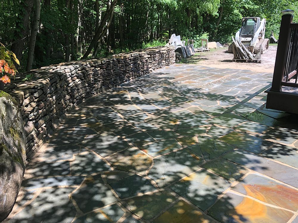 A stone wall surrounds a patio in a backyard.