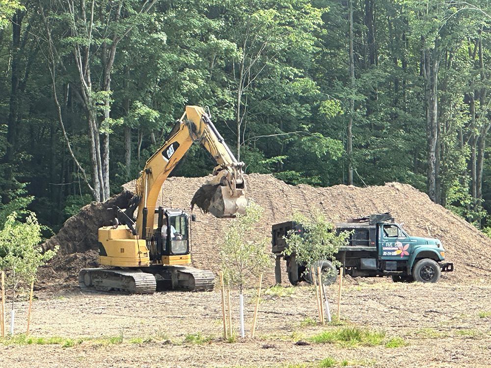 A bulldozer is moving dirt in a field next to a dump truck.