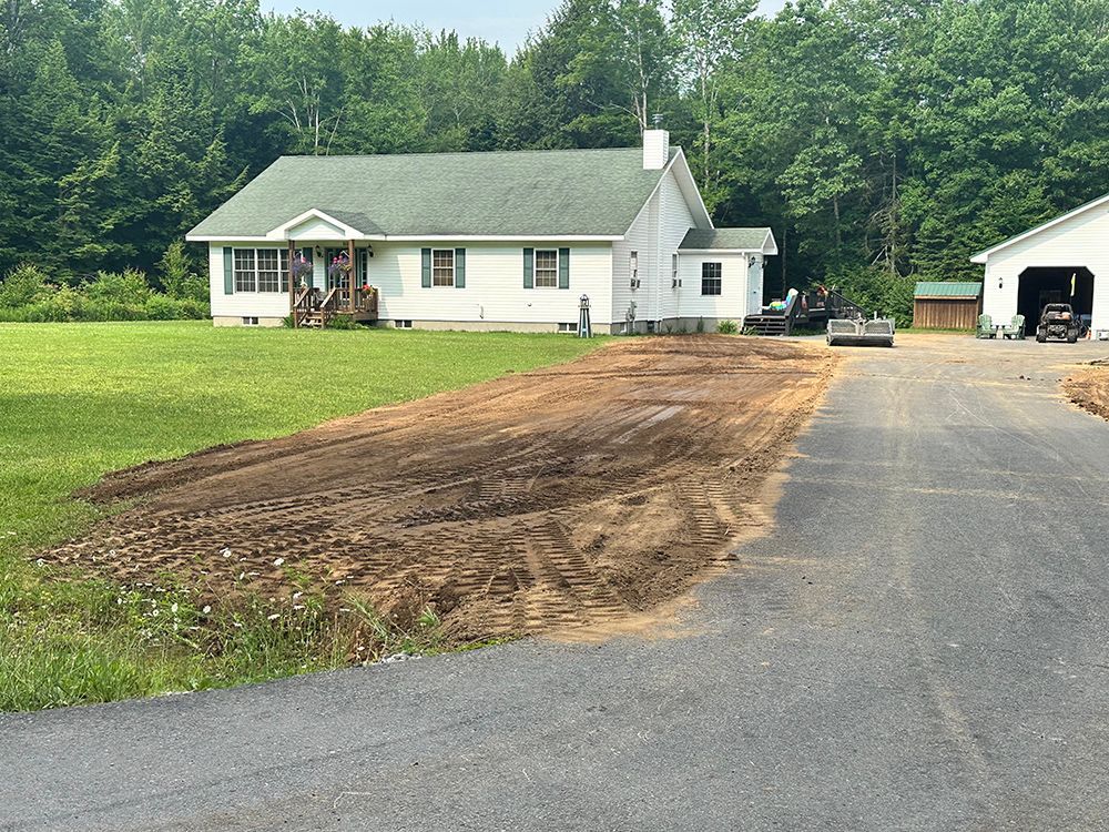 A white house with a green roof is next to a dirt road