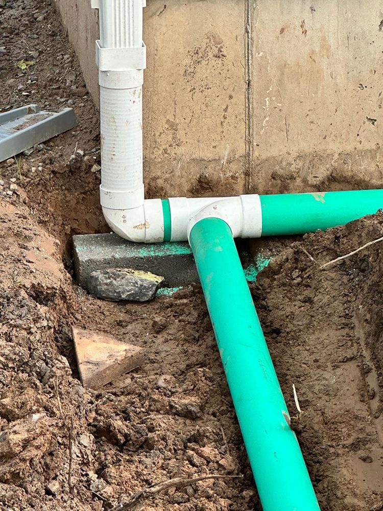 A green pipe is sitting in the dirt next to a white pipe.